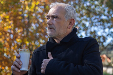 Fototapeta premium man with coat having a coffee in the park in autumn