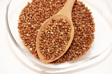 small brown buckwheat grains in a transparent glass plate and in a wooden spoon
