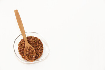 small brown buckwheat grains in a transparent glass plate and in a wooden spoon