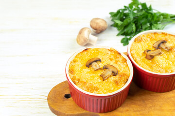 Chicken and mushroom casserole with golden crust, julienne with baked cheese, creamy gratin in portion ramekin clay pot on white wooden background. French cuisine. Top view, flat lay with copy space