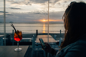 Une femme buvant un cocktail au bord de la mer. Un cocktail et un coucher de soleil. Une femme...