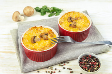 Chicken and mushroom casserole with golden crust, julienne with baked cheese, creamy gratin in portion ramekin clay pot on white wooden background. French cuisine. Top view, flat lay with copy space