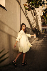 Full length pretty young caucasian girl posing looking at camera standing on street. Brunette is resting in summer evening weather. City life concept