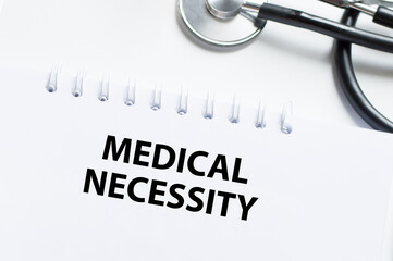 Medical Necessity text on a notebook on a light desk next to it is a stethoscope