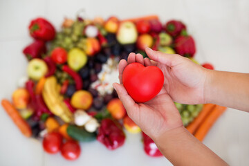 Serce trzymane w dłoniach na tle różnokolorowych owoców, dbanie o zdrowie, dieta złożona ze świeżych ooców - obrazy, fototapety, plakaty