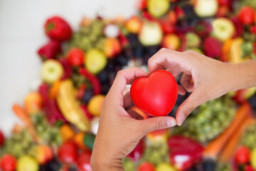 Serce trzymane w dłoniach na tle różnokolorowych owoców, dbanie o zdrowie, dieta złożona ze...