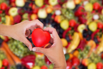 Serce trzymane w dłoniach na tle różnokolorowych owoców, dbanie o zdrowie, dieta złożona ze świeżych ooców