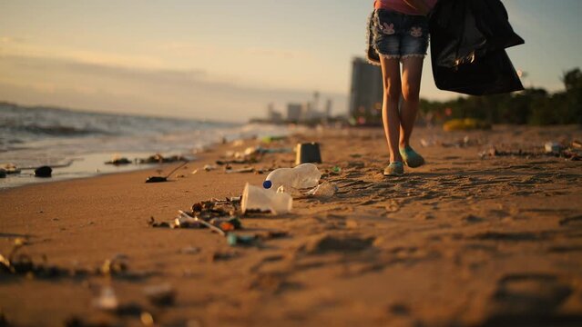 Woman under picking up plastic bottle garbage environment pollution cleaning up on the beach is volunteer concept with sunset sky background.