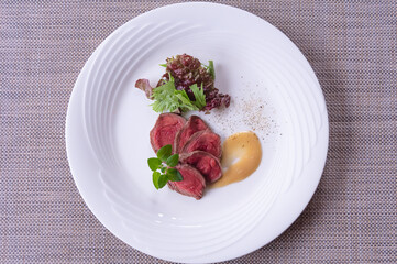 網目状のテーブルマットの上の白い皿に盛りつけた牛肉のロースト。