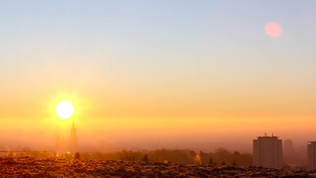 Sun is rising above Ulm and crossing Ulm minster. The city is covered with mist and some high buildings of Eselsberg are visible