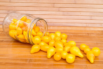 Small yellow tomatoes spilled out of a glass jar. Closeup image of yellow pear tomatoes. Organic healthy food.
