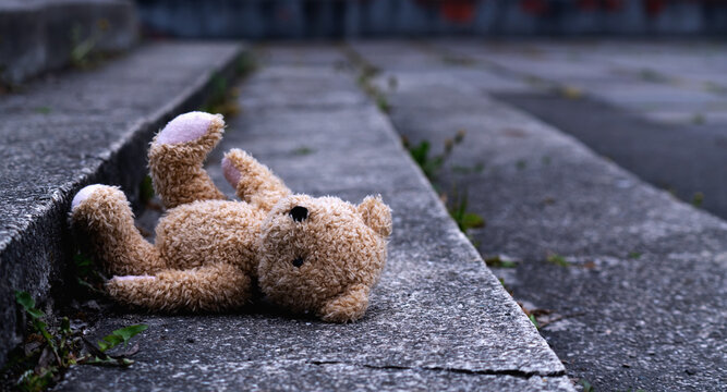 Conceptual image: loss childhood. Dirty teddy bear toy lies outdoors on the road as symbol of childrens loneliness