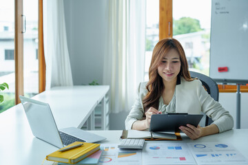 A portrait of a businesswoman holding a budget document and using computers and calculators placed...