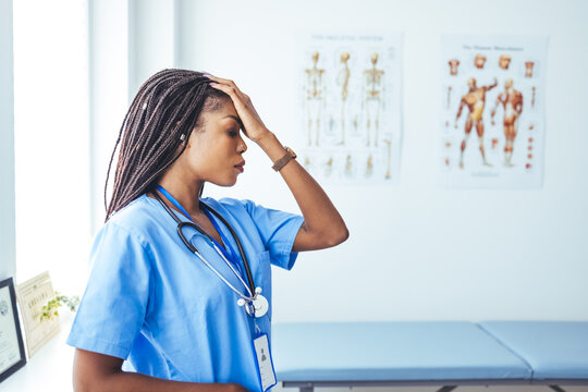 Shot of a young female nurse looking stressed out while standing at a window in a hospital. Tired female nurse in hospital corridor. Female nurse suffering from headache