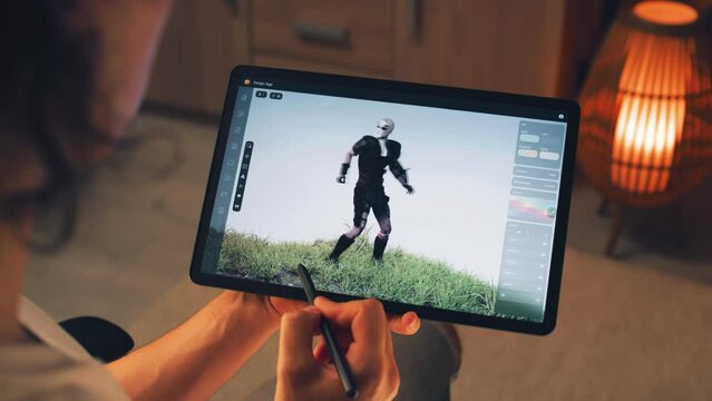 Male 3D designer creating 3D animation of video game character in design application on modern digital tablet computer using stylus