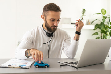 The man in the suit working in the office at a laptop, holding a car paying with a credit card. The concept of finding and buying cars on the Internet