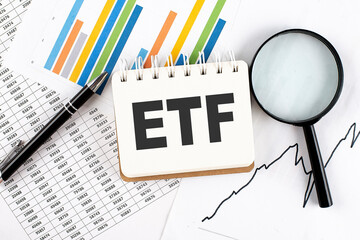 ETF text on notebook on the graph background with pen and magnifier