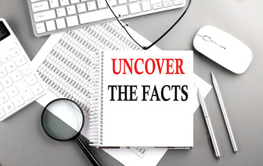 UNCOVER THE FACTS text on notepad on chart with keyboard and calculator on grey background