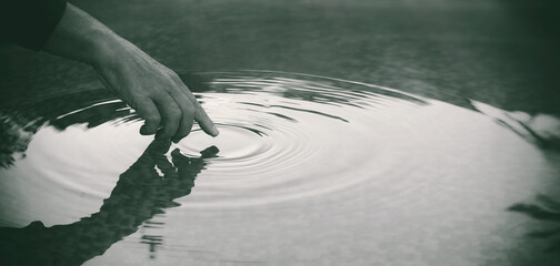 Detail of a hand touching lake water surface leaving ripples in concentric circles. People in nature. Unity, harmony and mindfulness concept