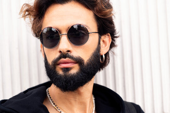 close up portrait of a beautiful young man with beard and sunglasses in a white background, concept of urban lifestyle and stylish clothing