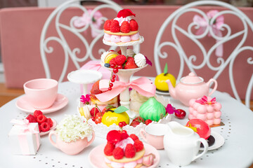 Abundant assortment of sugar dessert treats with present box and teapot on white table with chairs in cafe or restaurant