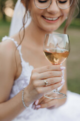 Vertical portrait of cropped smiling bride in wedding dress and veil with glasses drinking bubbly champagne in wineglass