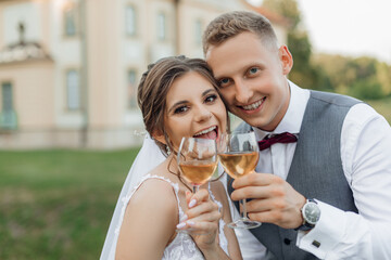 Cheerful, laughing married couple of bride in wedding dress and groom in suit drinking and toasting champagne glasses