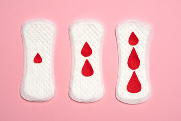 Three panty liners with red drops, on pink background.