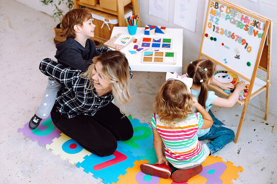 Teacher with children having fun and playing games, learning letters and numbers in kid development childcare center 
