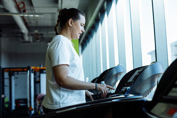 Adult plus size woman run on modern treadmill at fitness gym, side view. Middle aged lady set up...