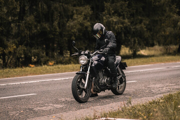 Fototapeta na wymiar male motorcyclist in a warm jacket and helmet in cold autumn weather on the road with a motorcycle cafe racer