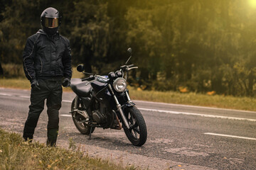 Obraz na płótnie Canvas male motorcyclist in a warm jacket and helmet in cold autumn weather on the road with a motorcycle cafe racer