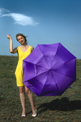 woman in yellow sundress with purple umbrella on the meadow against the blue sky and cloud