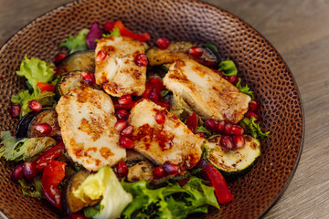 Fresh chicken breast fillet salad with pepper, basil, eggplant and garnet on plate on wooden table in cafe or restaurant
