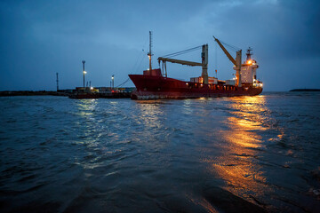 Fototapeta premium Cargo ship near the pier. Evening industrial seascape. Sea freight and supply in the North-East of Russia. Anadyr estuary, Chukotka, Russian Far East.
