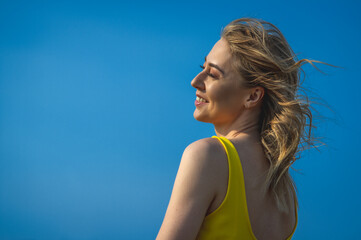 closeup sideview of smiling attcative caucasian woman in yellow sundress looking side against ultramarine sky