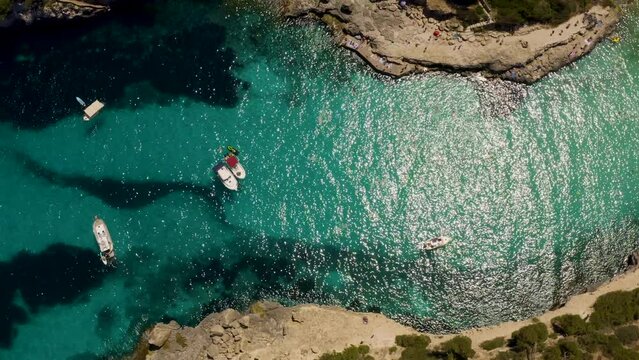 Aerial top down shot in 4k of yacht in crystal clear blue and turquoise Mediterranean Sea in Mallorca, Spain - Luxury Holiday - Balearic Islands