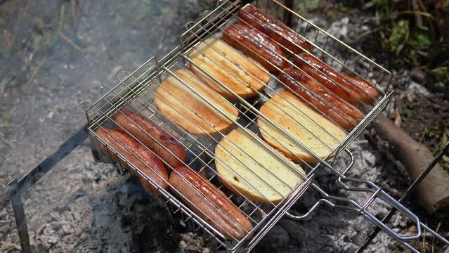 Grilling sausages with white bread slices in grill grate. The concept of resting in the fresh air, frying sausage on the grill, BBQ. Roasting on the fire barbecue. Hot smoke passes through products