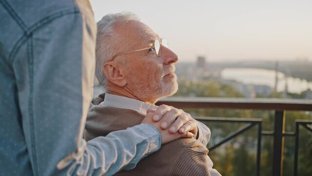 Woman puts hands on shoulders of disabled senior father