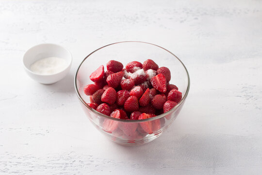Glass bowl with chopped strawberries and sugar on a light blue background