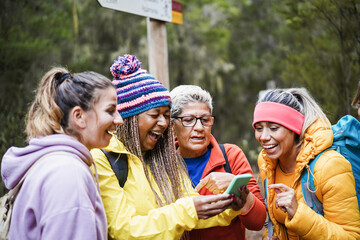 Multiracial women having fun with mobile phone during trekking day in mountain forest - Focus on...