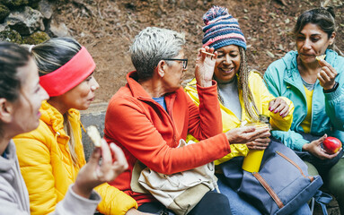 Multiracial women having fun taking a break after trekking day in mountain forest - Focus on center woman face
