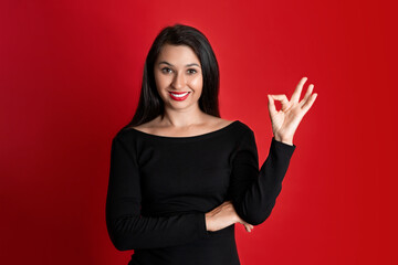 Studio emotional Portrait of a Beautiful Young Woman in a Black Dress with Red Lipstick on Her Lips. Red colored background. place for text