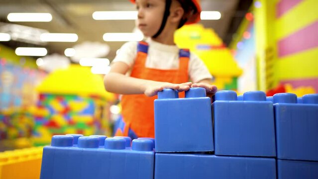 Happy boy wearing safety hardness and work helmet playing as an engineer in modern entertainment center playroom. Developing kids imagination concept.