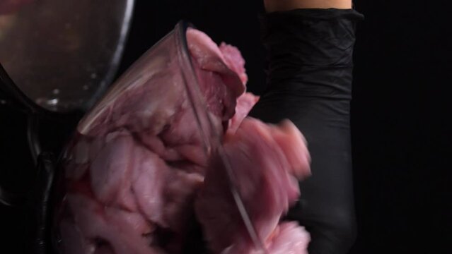 Vertical video. A cook in black gloves transfers raw pork from a glass bowl to a stainless steel pan. static general frame from the side.