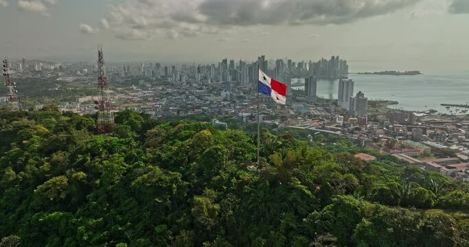 Panama City Aerial v67 cinematic low level flyover ancon hill with wind blowing the national flag on hilltop with coastal downtown cityscape in the background - Shot with Mavic 3 Cine - March 2022