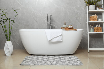 Fototapeta na wymiar Soft bath towel and personal care products on tub tray in bathroom