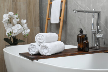 Fototapeta na wymiar Rolled towels and personal care products on tub tray in bathroom