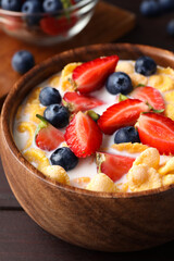 Bowl of tasty crispy corn flakes with milk and berries on wooden table, closeup
