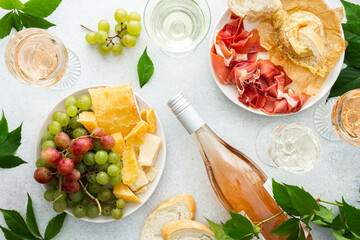 Top view of table with rose and white wine in glasses, plates with grapes, cheese and jamon, baked...
